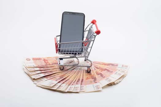 Against the background of five thousandth bills, there is a grocery cart with a phone