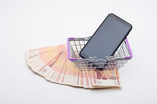 Against the background of five thousandth bills is a grocery basket with a cell phone