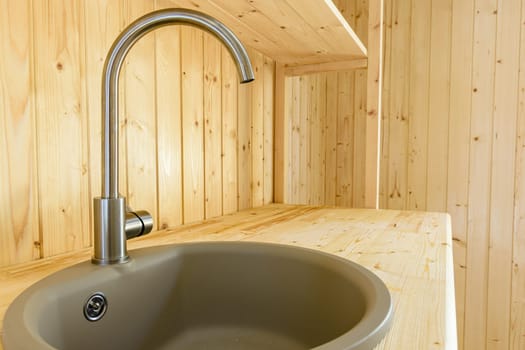 Sink with a mixer close-up in a kitchen set made of natural wood