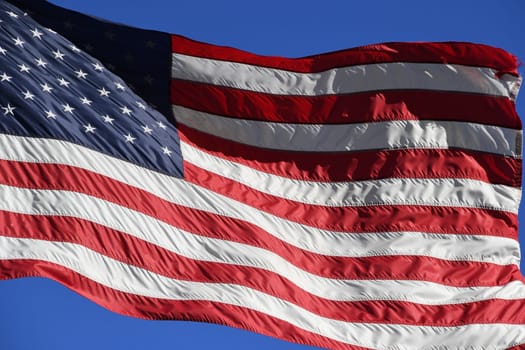 The American flag is waving in the wind. Stars and stripes can be seen on the USA flag.