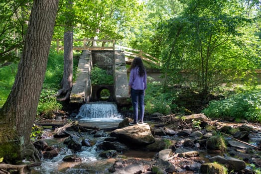 Young man stands on a rock at the base of a forest waterfall