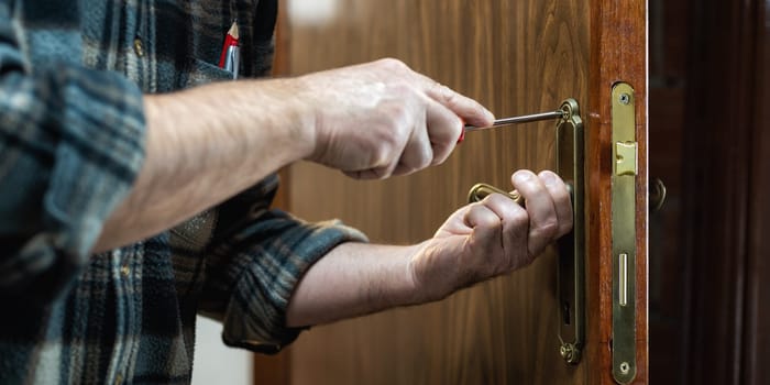 Close-up. Carpenter with screwdriver fixes the lock handle of a wooden door. Construction industry.