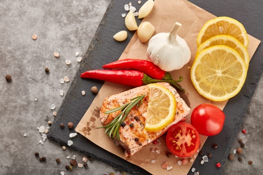 Grilled salmon fillet with spices and vegetables lying on stone cutting board on a grey background. Top view. Seafood menu.  Keto diet.