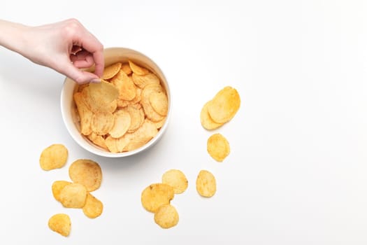 Hand with potato chips and bowl on white background. Junk food dedication concept. Top view, overhead