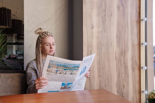 Attractive young hipster woman reading a newspaper at cafe
