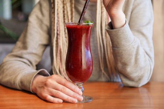Glass of smoothie cocktail made of blackberry, blueberry, strawberry and vanilla in woman's hands.