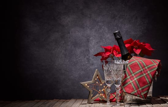 Champagne bottle in bucket with ice, empty champagne flutes and Christmas ornament on dark background with copy space. Christmas. New Year. Design element for greeting card, invitation, advertising