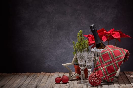 Champagne bottle in bucket with ice, empty champagne flutes and Christmas ornament on dark background with copy space. Christmas. New Year. Design element for greeting card, invitation, advertising
