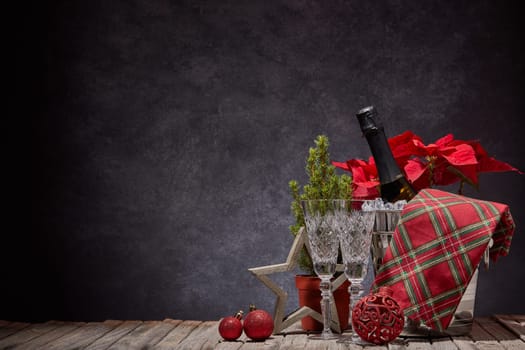 Champagne bottle in bucket with ice, empty champagne flutes and Christmas ornament on dark background with copy space. Christmas. New Year. Design element for greeting card, invitation, advertising