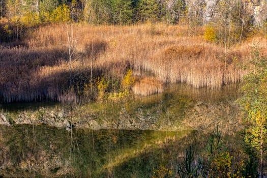 Beautiful reflection of autumn colored trees in water, landscape of abandoned and flooded s,all quarry, Czech Republic