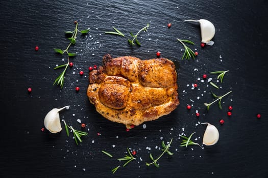 Grilled pork steak with spices, herbs and garlic on black background