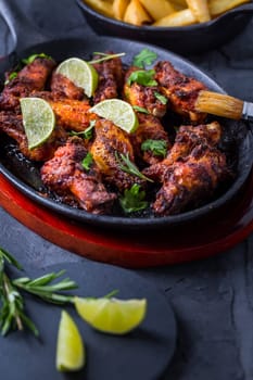 Roasted chicken wings in barbecue sauce with lime and baked potatoes in rustic pan