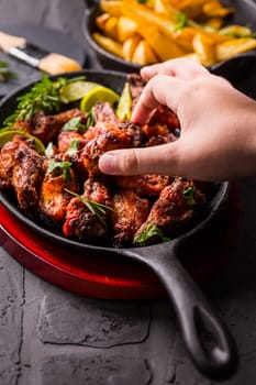Hand swiping roasted in barbecue sauce with lime and baked potatoes in rustic pan
