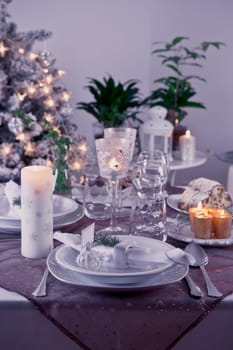 Table setting for celebration Christmas and New Year Holidays. Festive table at home with Christmas tree in violet tone.