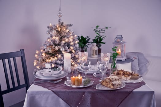 Table setting for celebration Christmas and New Year Holidays. Festive table at home with Christmas tree in violet tone.