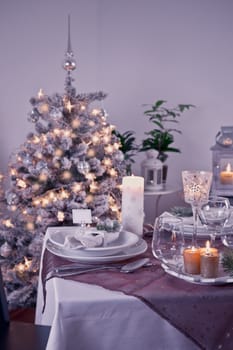 Table setting for celebration Christmas and New Year Holidays. Festive table at home with Christmas tree in violet tone.