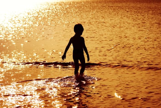 Children silhouettes in the water at sunset