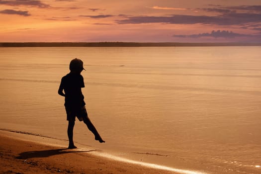 Boy walking on the beach in summer evening