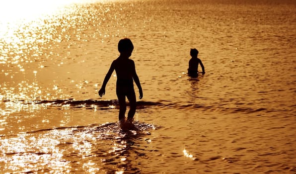 Children silhouettes in the water at sunset