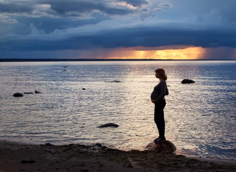 Pregnant woman standing at sunset on the coast