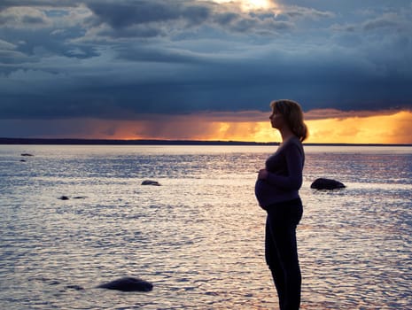 Pregnant woman standing at sunset on the coast