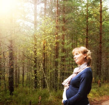 Pregnant woman standing in forest in morning light