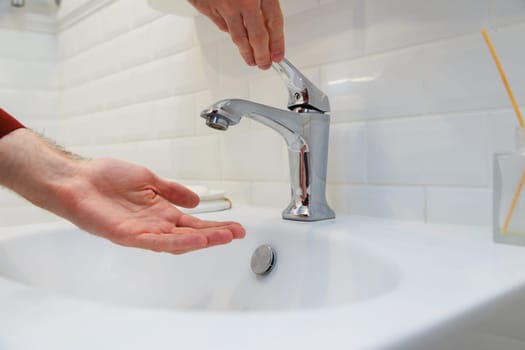 Man holding his hand under opened tap without water. Shutdown of water supply for non-payment or during repair work of the central system