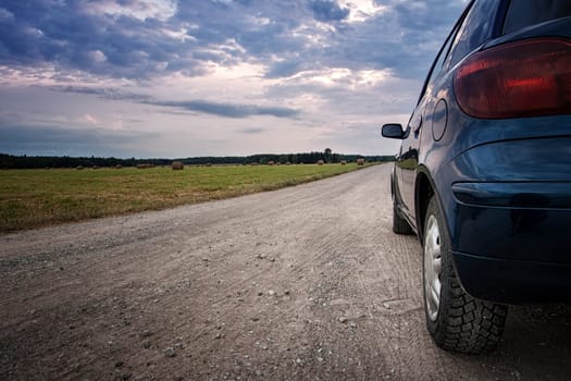 Car on country road at cloudy sunset