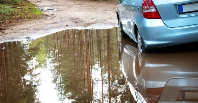 Car on dirt road with wheels in big puddle