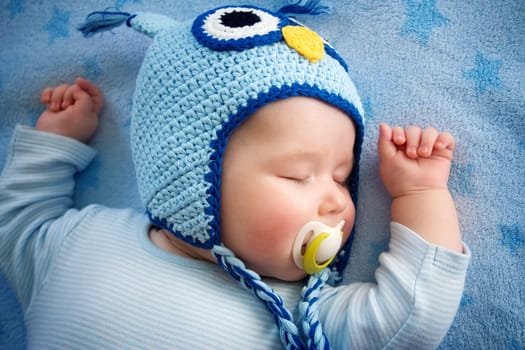 4 month old baby in owl hat sleeping on blue blanket
