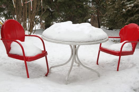 Two red art deco chairs around white table in winter with snow on table