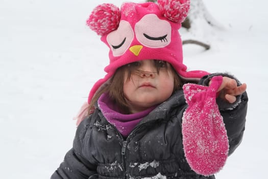 Little girl in pink winter hat holding a lost mitt i midst of falling snow