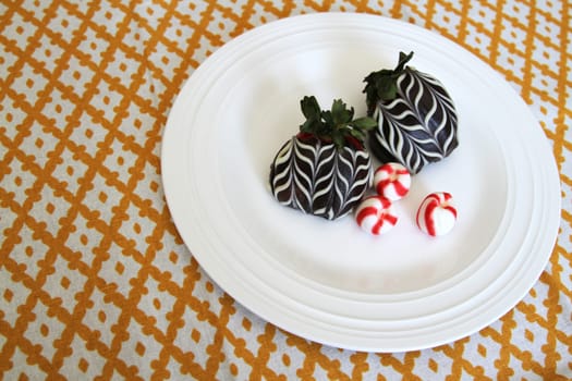 Chocolate covered strawberries with red and white peppermint hard candies on a plate on gold checkered tablecloth