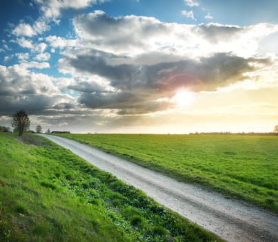 Evening country road with dramatic sky and green field