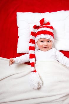 Baby in red and white hat on the bed