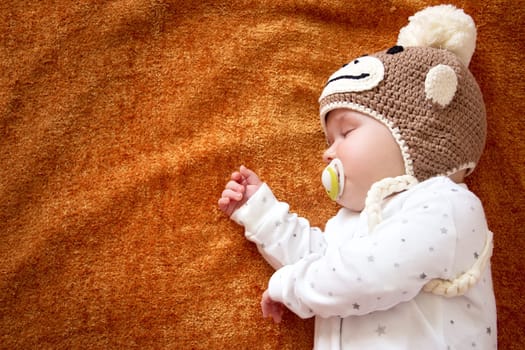 little baby in knitted montey hat on brown blanket