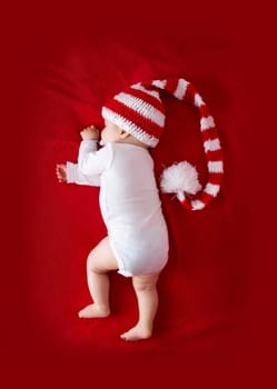 Little baby in knitted red whitey hat on red blanket