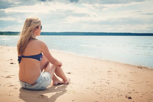 young woman sitting on the beach in sunglasses