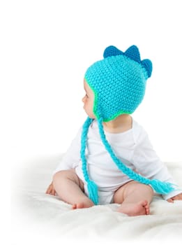 little baby in knitted dinosaur hat on soft blanket