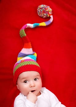 Baby in red and white hat on the bed