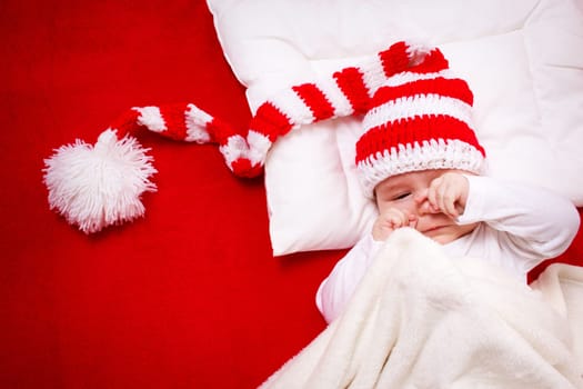 Sleepy baby on red blanket in knitted hat
