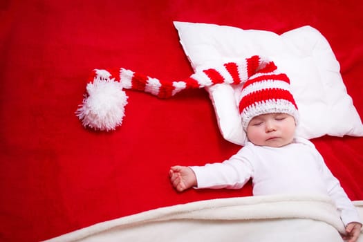 Sleepy baby on red blanket in knitted hat