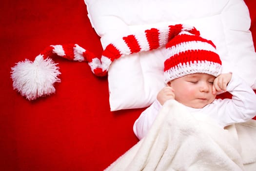 Sleepy baby on red blanket in knitted hat
