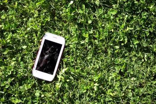 Smartphone with broken screen lying on green grass