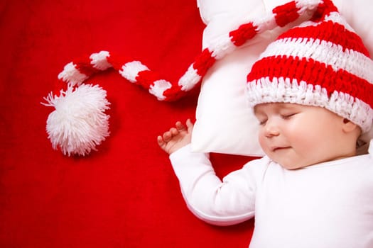 Sleepy baby on red blanket in knitted hat