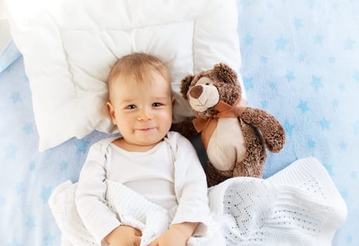 One year old baby lying in bed with a plush teddy bear
