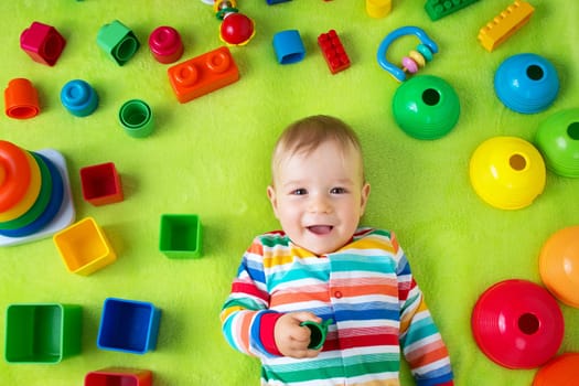 Baby boy lying on green blanket with many toys around