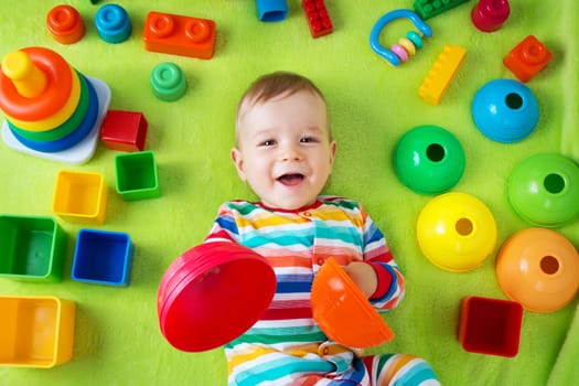 Baby boy lying on green blanket with many toys around