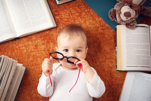 One year old baby among books with spectackles and a teddy bear
