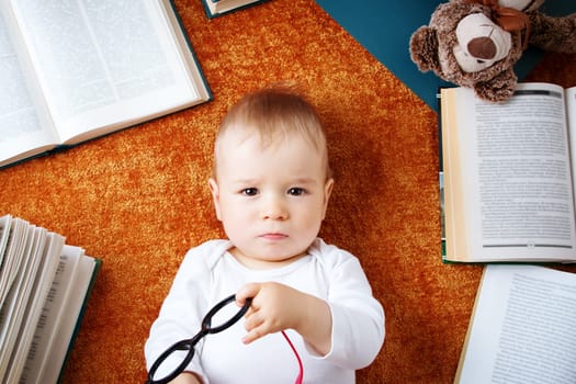 One year old baby among books with spectackles and a teddy bear